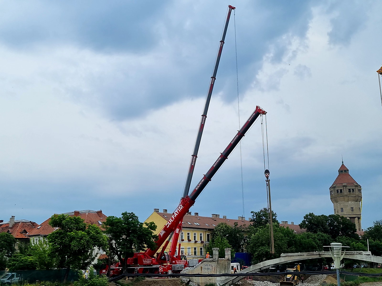 Pasarela Gelu: Automacara Liebherr Sulfatim pozitionata langa pasarela, cu turnul de apa si centrul vechi al Timisoarei in fundal.